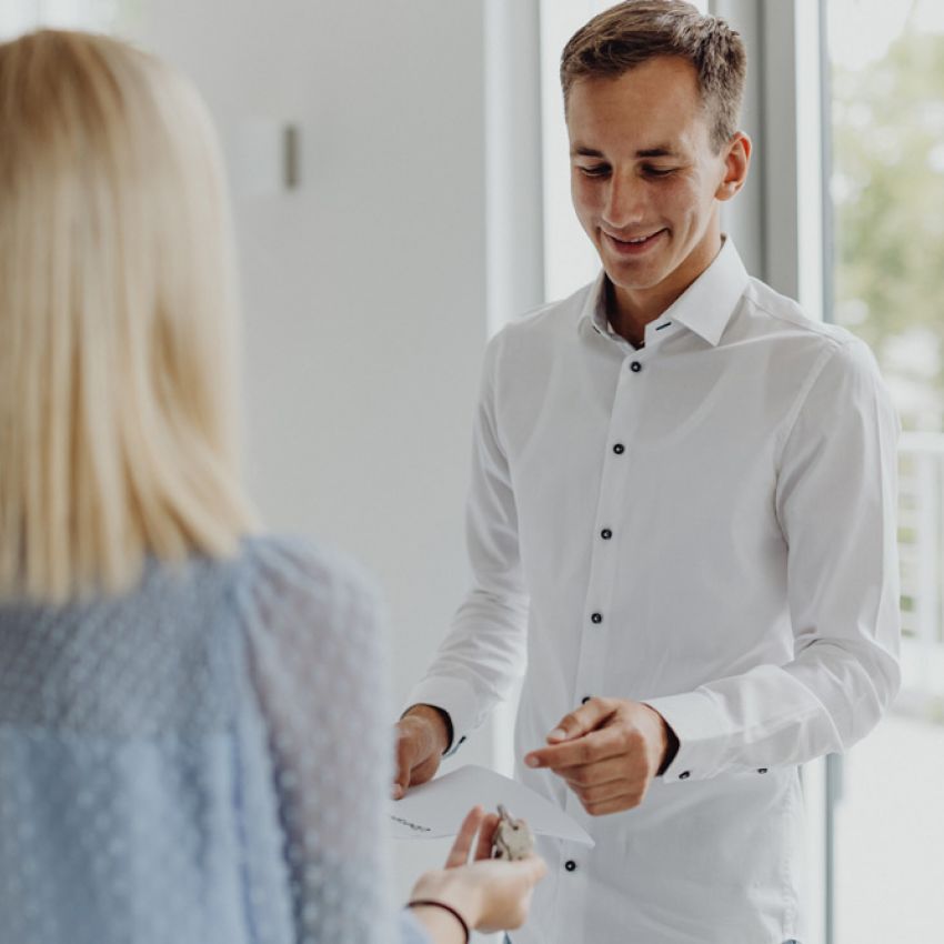 Mitarbeiter übergibt einer Kundin freundlich Dokumente in modernem Büro