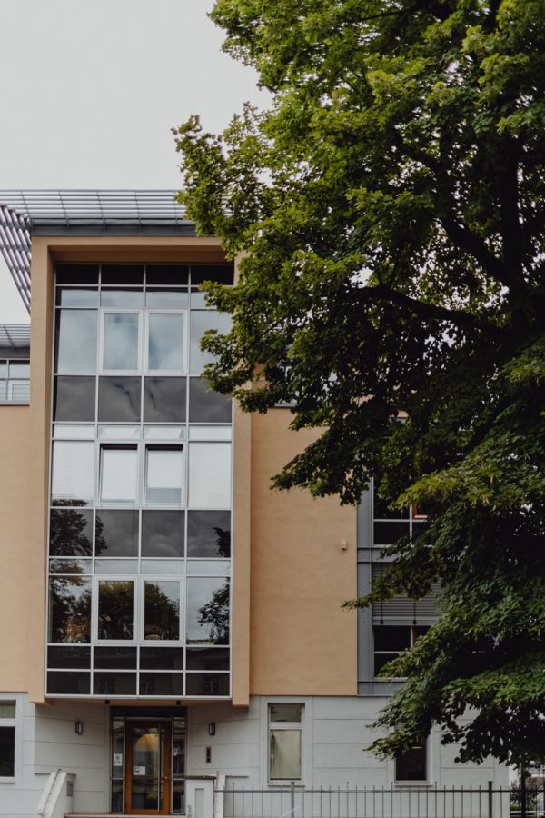 Modernes Wohn- und Geschäftsgebäude mit großflächigen Glasfronten und hellem Fassadenanstrich, teilweise von einem Baum verdeckt.